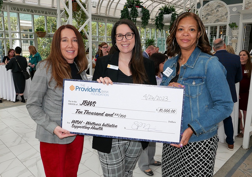 Three women stand facing the camera, holding a giant check for $10,000