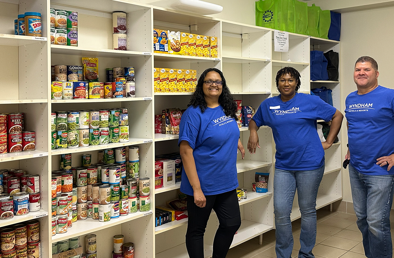 Three people stand in front of white shelving unit filled with cans of food